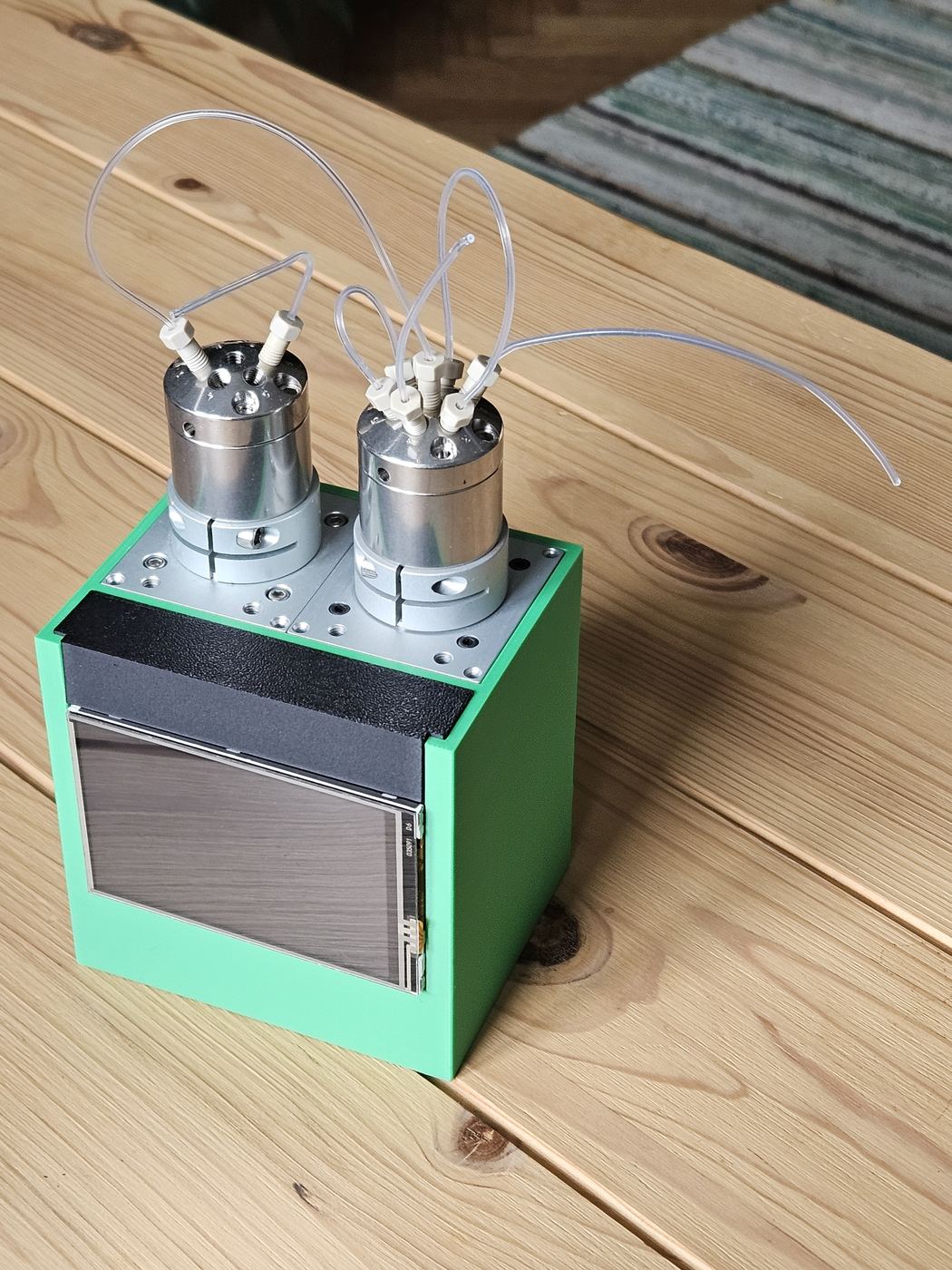 A first green enclosure with a screen at the front and two valves with tubing on top, on a wooden table
