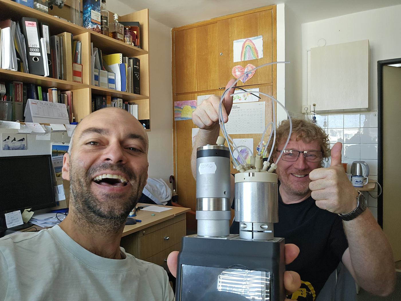 Selfie of David Cocovi-Solberg and Burkhard Horstkotte, smiling and giving a thumbs up, holding the second prototype in an office